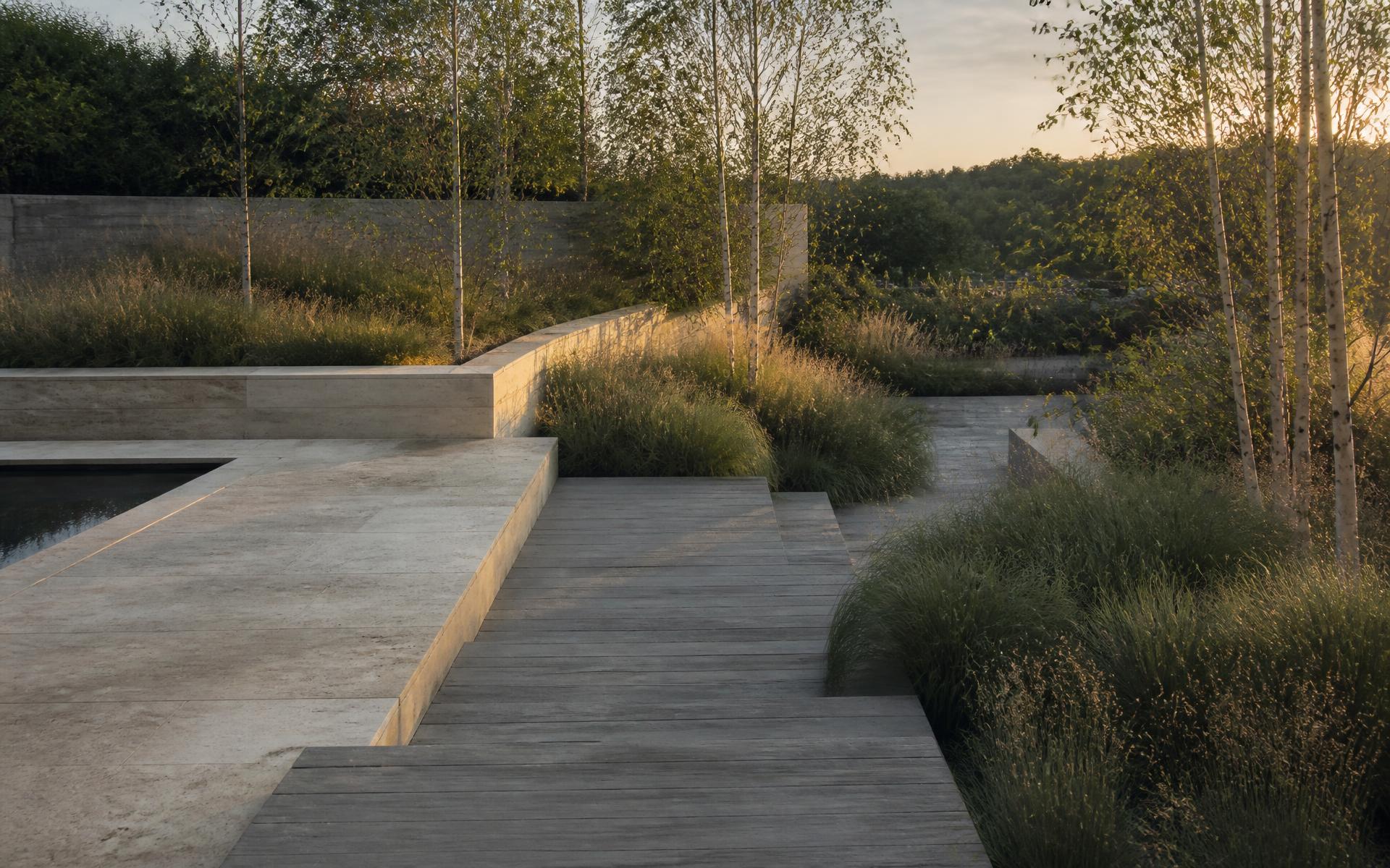Limestone terrace stepping down into ornamental grasses and birch trees at golden hour.